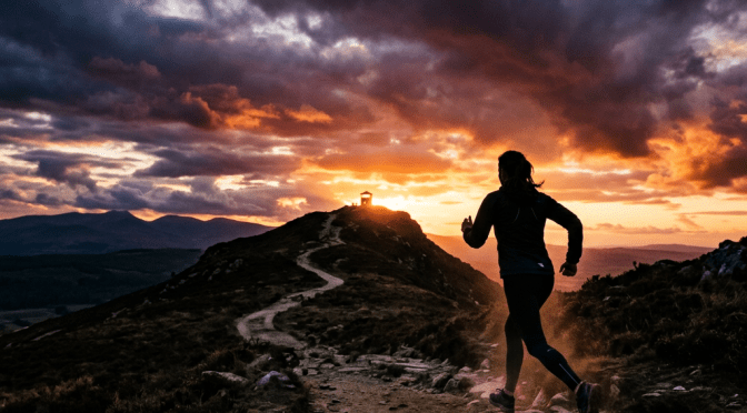 Silhouette of a runner on a rocky trail heading up a hill with a colorful sunset sky