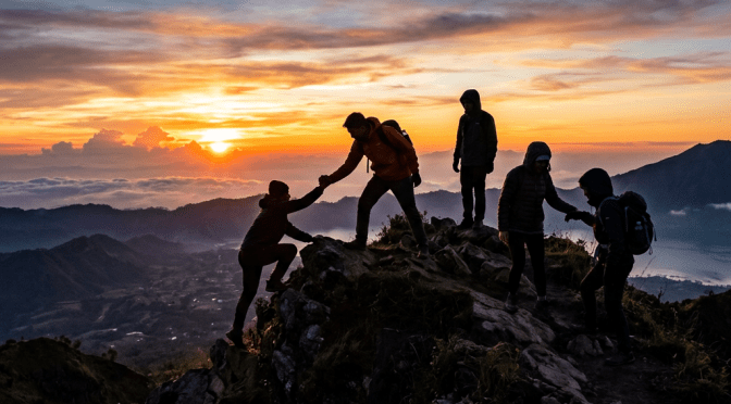 Group of hikers assisting each other on rocky ridge at sunrise