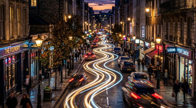City street at night with light trails from moving cars and pedestrians on sidewalks